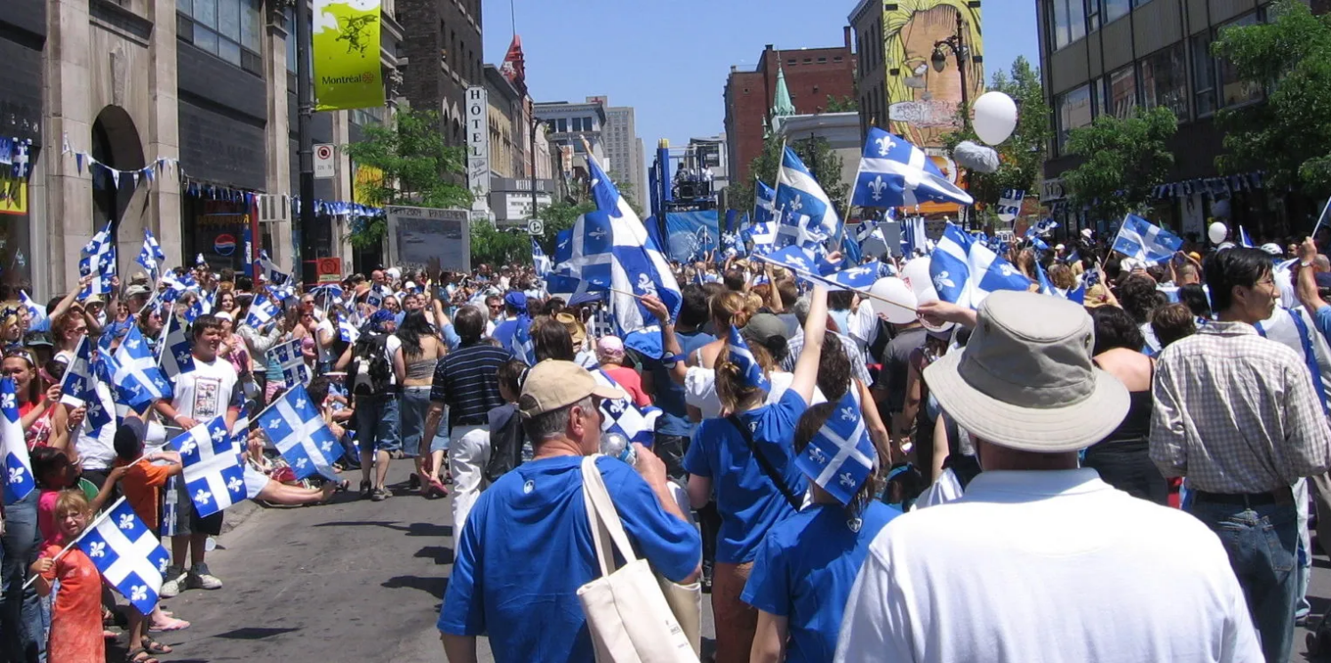 Foto mostrando várias pessoas desfilando na rua nas cores da bandeira do Québec